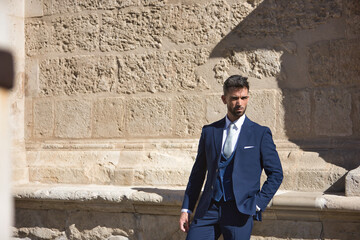 Attractive young businessman with beard and suit, posing next to a stone wall. Concept beauty, fashion, success, achiever, trend.