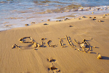 Close-up Of Inscription Word Sicily Written On Wet Sand Of Beach Seashore Coastline After Tide Near Waves At Sunset.