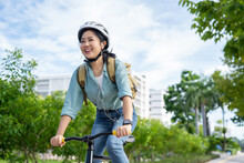 Happy Asian Woman Wearing A Helmet And Listening To Her Favorite Music While Riding A Bicycle Through A City Park.