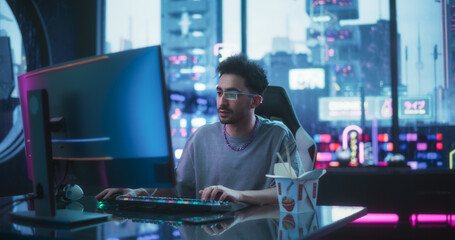 Handsome Young Man Eating Take-Away Asian Food, while Working on a Desktop Computer in a Cyberpunk Neon Room. Futuristic Hacker Writing Software Code and Wearing Innovative Augmented Reality Glasses