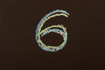 The number six is written on a black board with chalk of different colors.