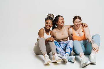 Wall Mural - Group of joyful women in sportswear hugging while sitting isolated over white wall