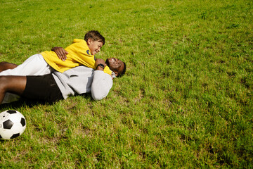 Wall Mural - African man hugging his adopted son while playing football together in park