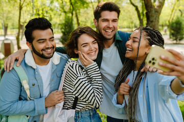 Wall Mural - Four smiling students taking selfie while spending time together in park