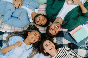 Wall Mural - Top view of group of positive friends students smiling while laying on blanket