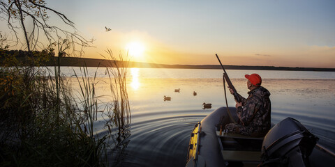 Wall Mural - Duck hunter at sunrise. Waterfowl hunter in boat at sunset. banner with copy space.