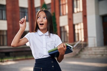 Thinking, having an idea. School girl in uniform is outdoors near the building