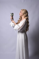 Wall Mural - Close up portrait of beautiful blonde model wearing elegant  white halloween gown, a historical fantasy character.  Holding wine goblet, isolated on audio background.