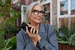 © Ivan Traimak - successful confident middle-aged woman dressed in a gray stylish jacket walks down the street and communicates using a smartphone