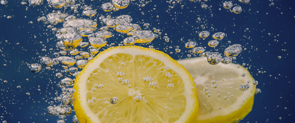 Poster - Underwater lemon slice in soda water or lemonade with bubbles. Refreshing soda tonic fizzy cocktail. Close up of lemons and ice cubes in glass. Lime in splashing sparkling water cold drink beverage.