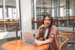 © Reezky - Smiling young Asian woman working remotely from cafe using her laptop, employee getting ready for online video-call interview