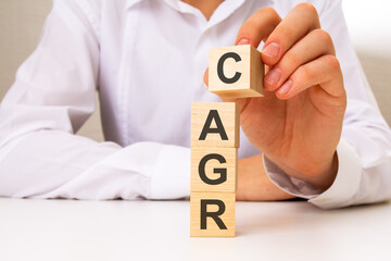 wooden cubes with the word CAGR, the hand puts a cube with letter C, business concept