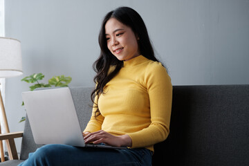 Young business freelance Asian woman working on laptop checking social media while lying on the sofa when relax in living room at home.