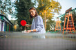 beautiful young woman playing table tennis in an amusement park. Playing ping pong outdoors.