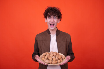 Wall Mural - A young attractive guy eats walnuts. Funny man posing on an orange background.