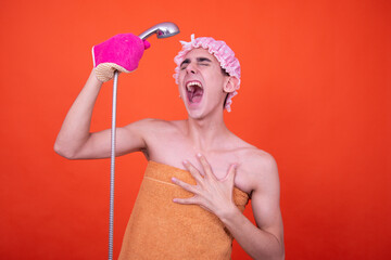 Wall Mural - A young attractive guy is washing himself in the shower. Funny man posing on an orange background.