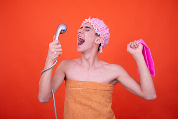 Wall Mural - A young attractive guy is washing himself in the shower. Funny man posing on an orange background.