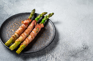 Wall Mural - Plate with pork bacon wrapped asparagus on grey table. White background. Top view. Copy space