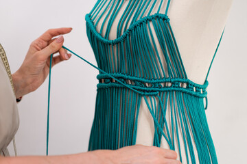 Wall Mural - Craftswoman braids macrame dress of green threads on mannequin in sewing atelier woman designer ties knot to make stylish apparel in dressmaking workshop closeup