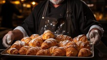 baker holding a metal tray full of fresh croissants