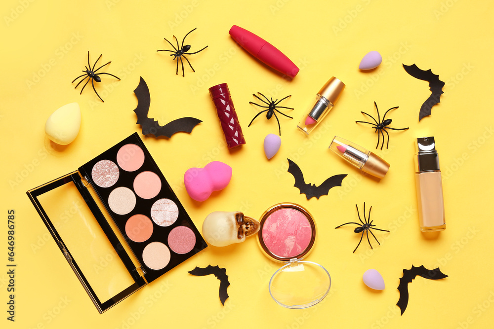 Lipsticks and different decorative cosmetics with Halloween decor on yellow background
