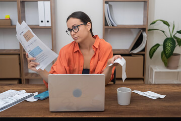 At home, a woman efficiently handles household utility bills online, laptop as her tool, clutching payment receipts securely