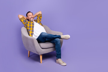 Poster - Photo of satisfied positive man hold arms behind head relax comfort trendy furniture empty space isolated on purple color background