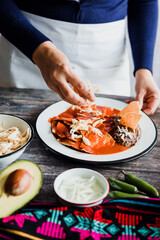 Wall Mural - Mexican woman hands preparing chilaquiles with red sauce and eating traditional mexican food for breakfast in Mexico Latin America