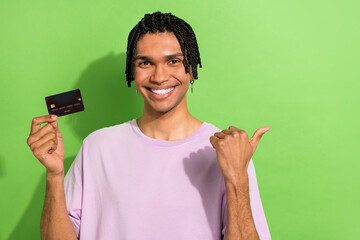 Poster - Photo of handsome guy beaming smile hold debit card indicate finger empty space isolated on green color background