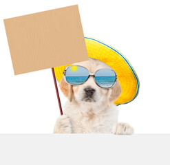 Poster - Funny Golden Retriver puppy wearing mirrored sunglasses and summer hat holds empty placard above empty white banner. isolated on white background