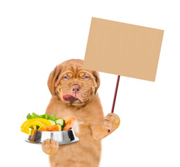 Aufkleber - Licking lips puppy holds bowl of vegetables and shows empty placard. isolated on white background