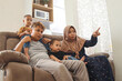 © Queenmoonlite Studio - Happy Asian muslim family with two children sitting on couch at home watching tv together