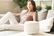 © KMPZZZ - Modern air humidifier during relax or rest, happy blurred asian young woman, girl enjoying aromatherapy steam scent from essential oil diffuser comfortable in living conditions room,apartment at home