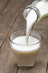 Canvas Print - milk pouring in glass from bottle on table