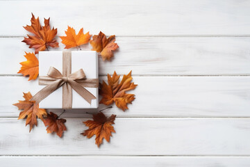 Gift box and maple leaves on white wooden background, top view, Thanksgiving and autumn background.