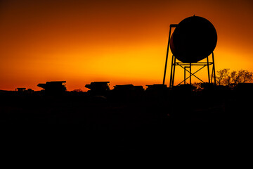 A silhouette of a water tower and mining trucks in the background at sunset