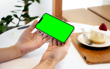 Poster - Person holding smartphone blank green screen modern design in cafe interior.