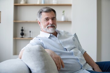 Wall Mural - Portrait of happy mature man sitting on sofa at home.