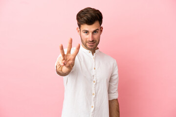 Wall Mural - Young caucasian handsome man isolated on pink background happy and counting three with fingers