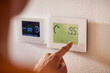 Ethnic woman adjusting smart thermostat control on wall