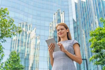 Business on the move. Digital banking on the go. Portrait of a young and successful white caucasian business woman using digital tablet standing in front of a modern cityscape of office buildings. 