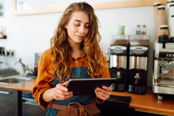 Smiling female barista takes an order from a panchette while standing at the bar counter in a coffee shop. Business concept. The concept of tenologies, takeaway food.