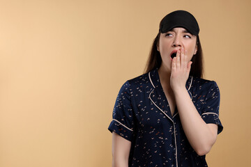 Canvas Print - Tired young woman with sleep mask yawning on beige background, space for text. Insomnia problem