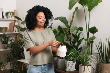 Canvas Print - Happy woman watering beautiful potted houseplants at home