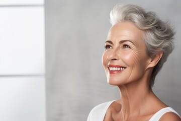 Portrait of a happy fifty year old woman with well-groomed facial skin on a gray background.