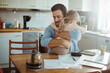 © Geber86 - Young single father finding hope in his daughters embrace while stressing over bills and home finances in the morning in the kitchen