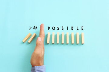 Poster - Male hand stopping the domino effect. Wooden cubes with the text impossible. Success and challenge concept