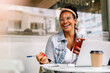 © (JLco) Julia Amaral - Happy female student sitting in a coffee shop, using a smartphone