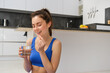 © Mix and Match Studio - Portrait of healthy, smiling young woman taking vitamins after workout, holding glass of water and dietary supplement, buds for health and energy