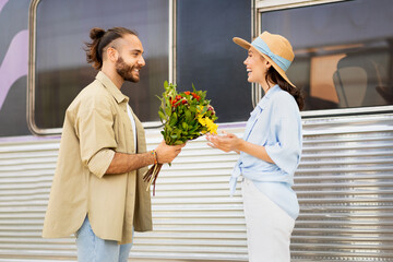 Cheerful young caucasian guy meets surprised woman, gives bouquet of flowers